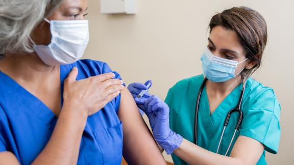 A masked healthcare worker administering a patient with the COVID-19 vaccine.