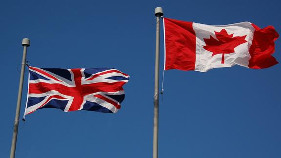 British flag on the left and an Canadian flag on the right on two seperate flag polls with the blue sky in the background.