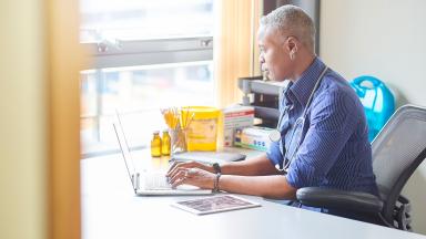 A general practitioner, typing, near a window.