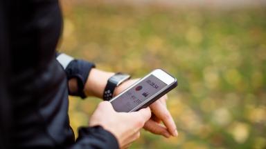 A runner wearing a smart watch, checking a health app on their phone.