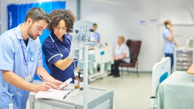 Healthcare staff on a ward, checking medicine against a computer.