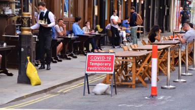 People dining outside by a sign which reads "COVID-19 temporary restrictions".