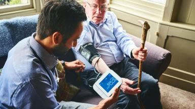 GP taking blood pressure of older man at home visit