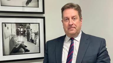 Jonathan Patton, Vice Chair, NICON, stood beside two wall-mounted black and white photographs