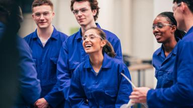 This image features a group of 5 NHS apprentices in blue boildersuits with their instructor.
