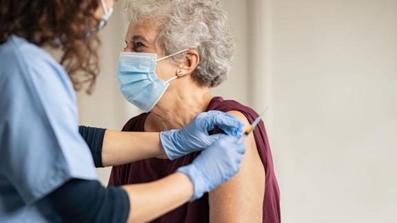 An elderly woman, wearing a mask, receiving the COVID-19 vaccine.