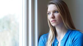 A concerned woman looks out of a window.