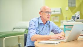 A doctor on a ward looking at a laptop.