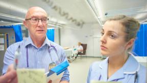 A doctor and a nurse check a board.