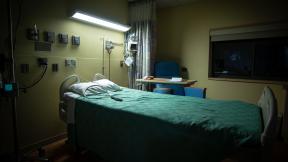 An empty hospital bed, on a ward at night time.
