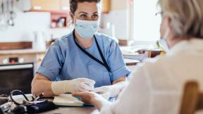 A community nurse in a mask, consulting a patient.