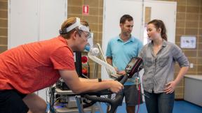 A man is hooked up to a machine monitoring his breath while he cycles.