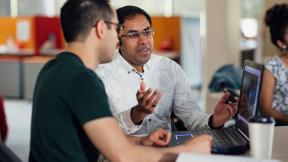 Office workers having a conversation and looking at a laptop.