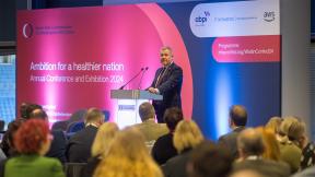 Jeremy Miles speaking in front of a seated crowd at the Welsh NHS Confederation Conference 2024.