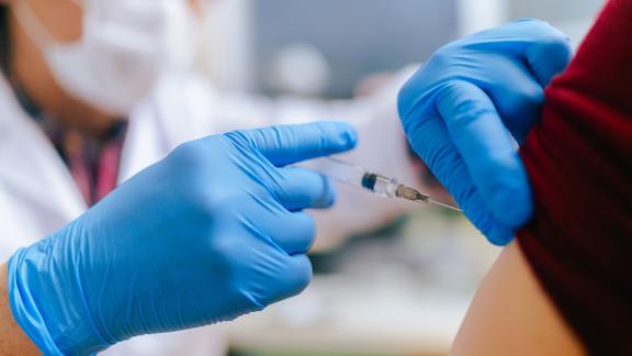 A healthcare worker wearing blue gloves administering the COVID-19 vaccine.