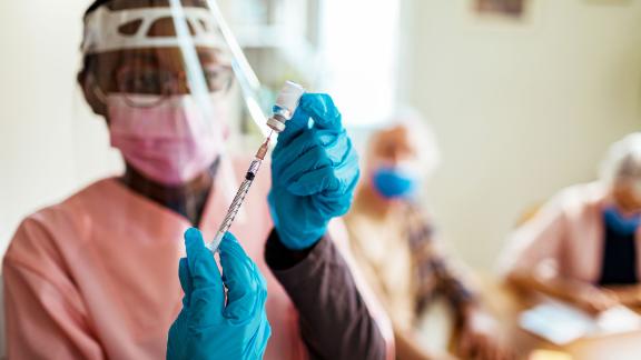 A healthcare worker in PPE, fills a syringe with a COVID-19 vaccination.