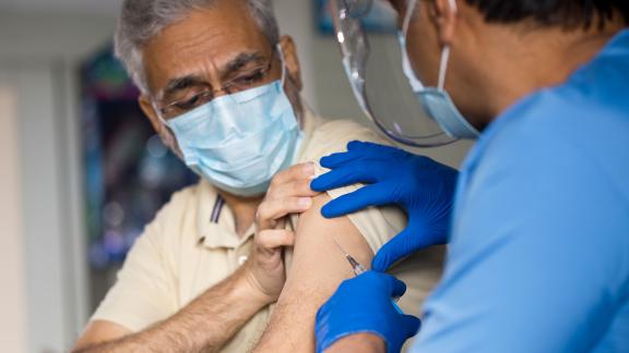 A healthcare worker wearing blue gloves administering the COVID-19 vaccine.