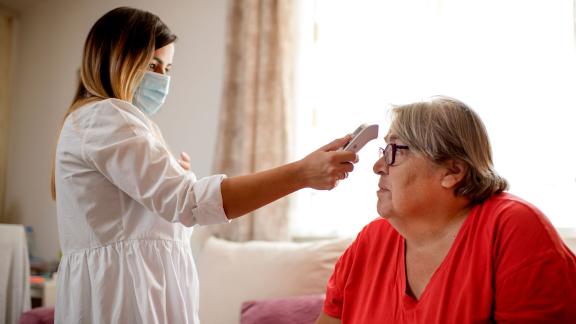 A masked care home assistant taking a resident's temperature.