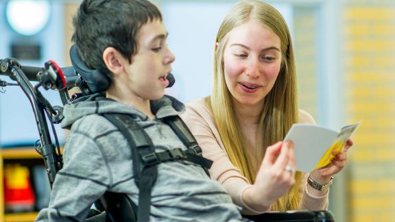 A child in a wheelchair being read to by a therapist.