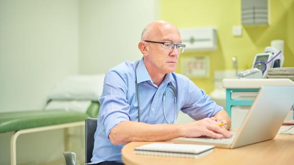 A doctor on a ward looking at a laptop.