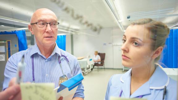 A doctor and a nurse check a board.