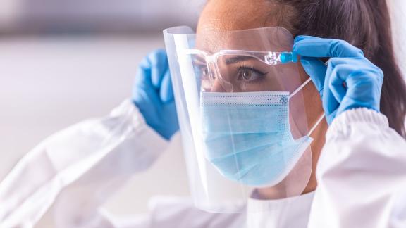 A healthcare worker wearing PPE, adjusting their mask and visor.