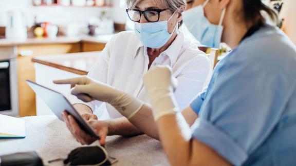 Masked healthcare workers point at a tablet computer.