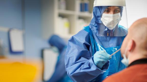 A healthcare worker in PPE takes a swab. 