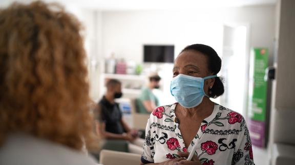 A masked patient talking to a receptionist.