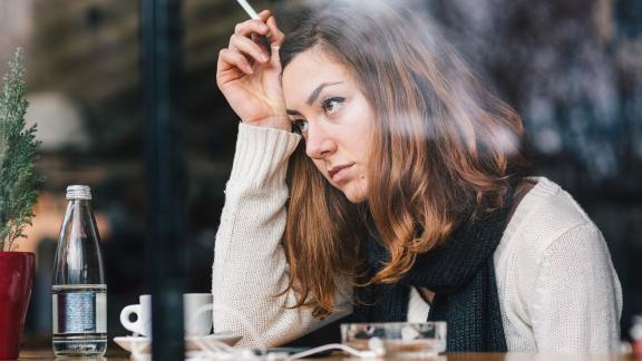 A troubled looking woman, smoking in a café window.