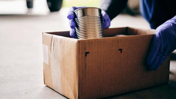 A tin can being put into a food bank box.
