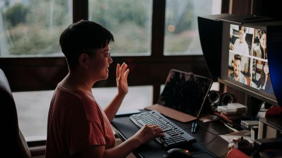 A woman waving to her colleagues on a video call.