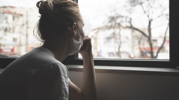 A woman wearing a mask looking out of a window.