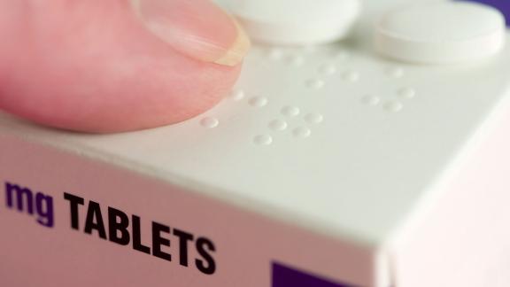 A finger touches braille on a box of tablets.