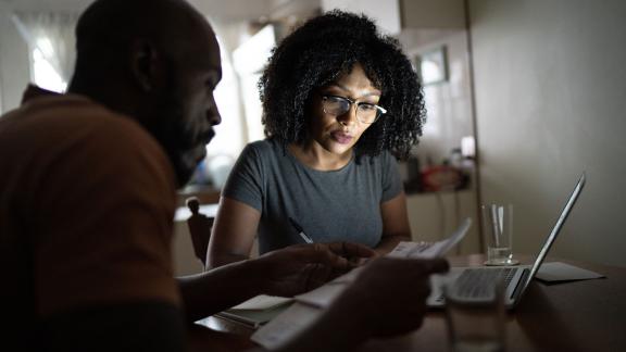 A couple discussing something, holding papers and near a laptop.