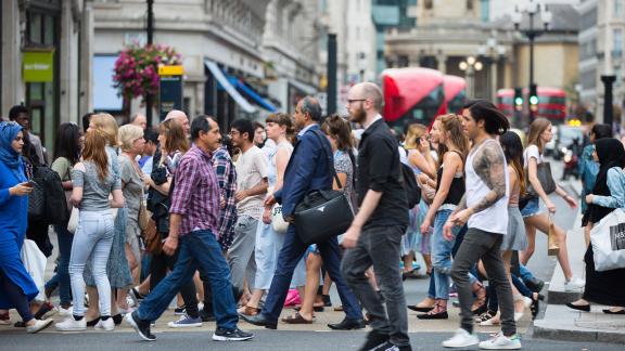 A crowd crossing a busy town centre street.