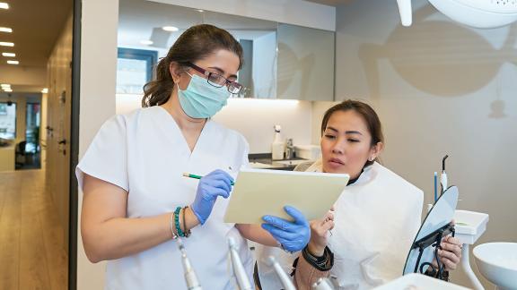 A masked dentist and patient having a conversation.