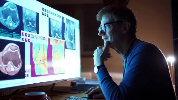 A doctor in a dark room checking scans on a screen.