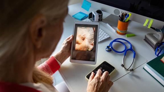 A GP holding a video call appointment and looking at a wound on a tablet screen.