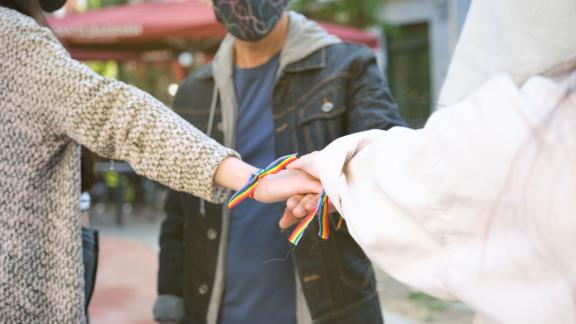 Hands of a group of three people with LGBT flag bracelets