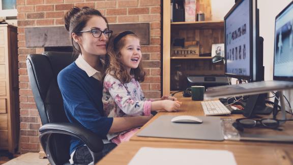 A mother on a video call while working from home, with their child on their knee.