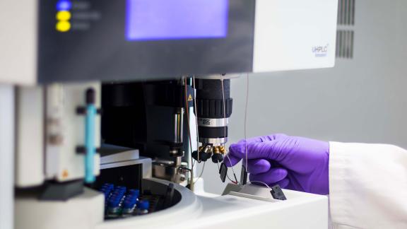 A gloved hand using a machine in a lab.