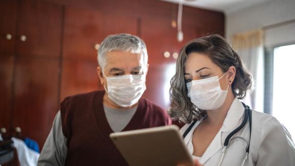 A masked doctor and patient looking at a laptop.