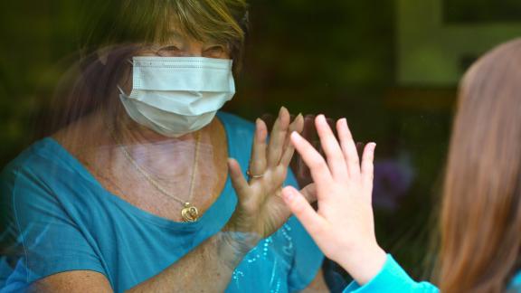 A grandmother and grandchild on either side of a window, touching fingers.