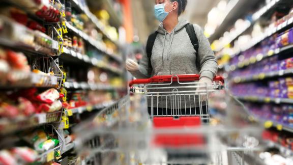 A masked woman pushing a trolley along a shopping aisle.