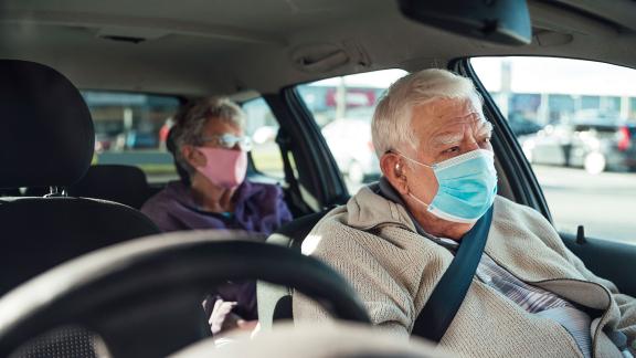 An older couple, wearing masks, are passengers in a car.
