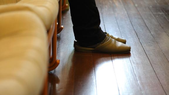 A close up of someone wearing slippers on a wooden floor.