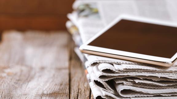 Stack of newspapers weighed down by a tablet