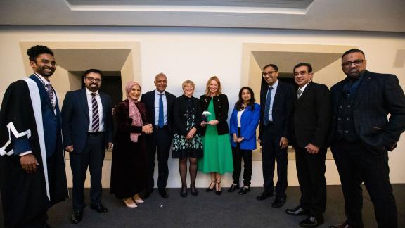 10 formally dressed award recipients stand in a row facing the camera and smiling