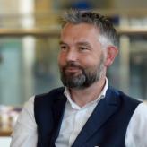 Accessibility description: A photo of Dr Jon Griffiths, a white man with greying hair and beard wearing a white shirt and black waistcoat and smiling.